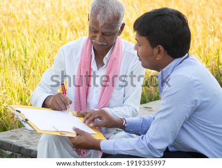 Selective focus on farmer, Banker or corporate officer getting sign from farmer while sitting near the farmland - concept of cotract farming, business deal and farm loan approval