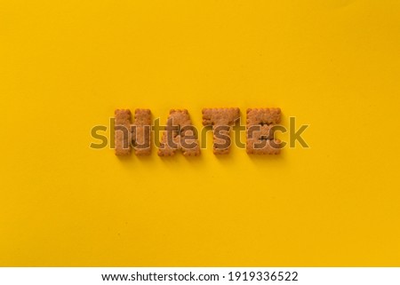 Word Hate in the middle of the picture made of tasty crunchy cookies in the form of English alphabet letters, textured bright yellow background, health, dieting and medical concept. Copy space