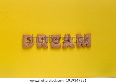 Word Dream in the middle of the picture made of tasty crunchy cookies in the form of English alphabet letters, textured bright yellow background, health, dieting and medical concept. Copy space