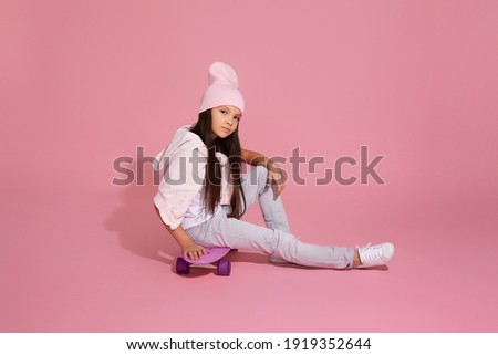 cute little child girl sitting on pink skateboard over pink background