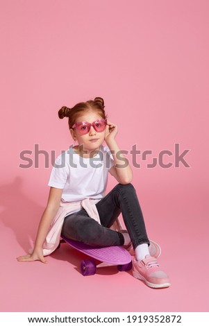 cute redhead little child girl sitting on skateboard, wearing pink sunglasses