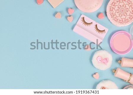Cute pink makeup beauty products like brushes, powder or lipstick on side of pastel blue background with empty copy space