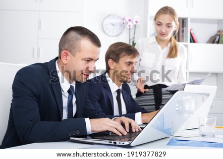 serious business male assistant wearing formalwear sitting with coworkers ay background in company office.