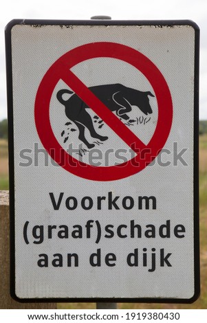 warning sign with Dutch text: prevent excavation damage to the dike, meaning do not allow your dog roam free or dig on the dike