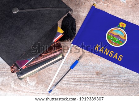 Black graduation hat on books next to Kansas flag, education concept, top view