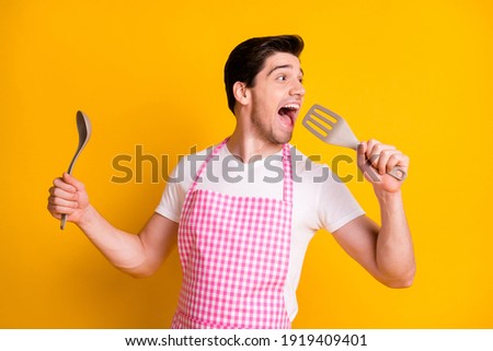 Photo portrait of funny man singing into spatula isolated on vivid yellow colored background Royalty-Free Stock Photo #1919409401