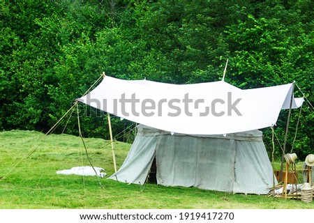 Old white big Bell tent standing on green meadow near forest. Vintage medieval tent by summer woods background Royalty-Free Stock Photo #1919417270