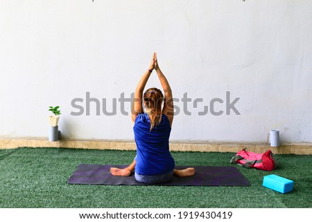 Female yoga instructor practicing seated Eagle Pose, Garudasana for exercise on yoga mat. Exercise for healthcare as lifestyle.
