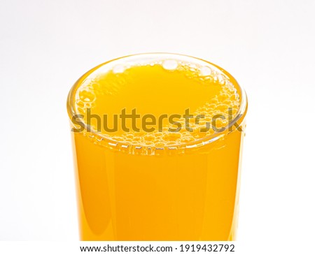 Close-up picture above bubbles of yellow orange juice in a circle glass drink natural refreshment white background isolated 