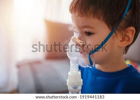 Little boy using inhaler at home. Cute caucasian boy inhaling with nebuliser. Image with selective focus. Home treatment. The boy makes inhalation with a nebulizer inhaling medicines into his lungs