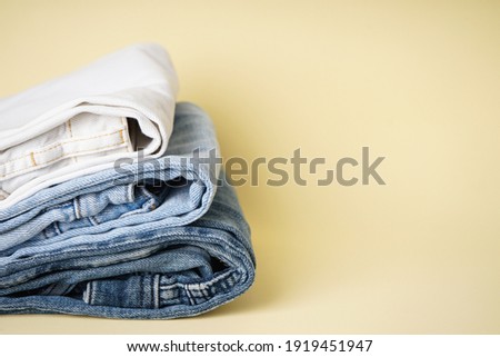 Stack different jeans on yellow background, space for text.