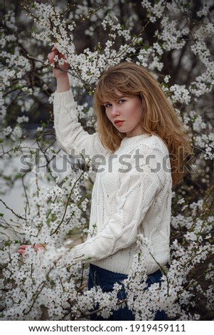 Pretty young woman in a white sweater in cherry blossom garden, spring time concept. Outdoor fashion photo