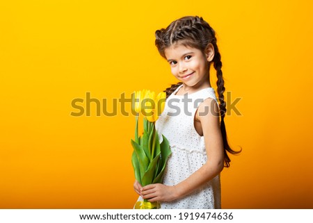 Cute little girl smiles in a yellow dress with tulips on a yellow background. Close-up. Space for text. The concept of spring. The concept of World Women's Day. March 8. The concept of spring discount