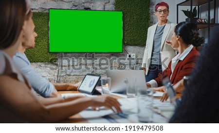 Office Conference Room Meeting: Female Chief Company Strategist Doing Green Screen TV Presentation to a Diverse Team of Multi-Ethnic Businesspeople. Using Chroma Key Wall TV Monitor