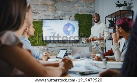 Office Conference Room Meeting: Black Chief Company Strategist Doing TV Presentation to a Diverse Team of Multi-Ethnic Professional Businesspeople, Explaining Marketing Strategy, Data Analysis Royalty-Free Stock Photo #1919479520