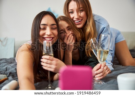 Smiling dark-haired lady taking pictures of herself and her high-spirited female friends with the cellphone