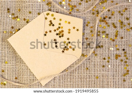 Cute craft paper envelope, scattered golden stars close up on gray linen background