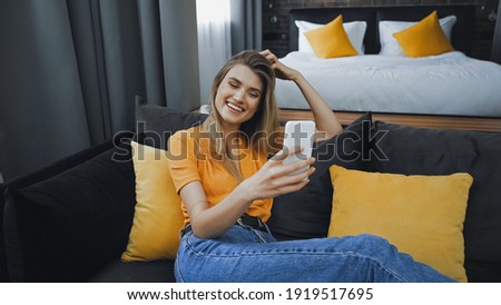 cheerful woman taking selfie on couch in hotel room
