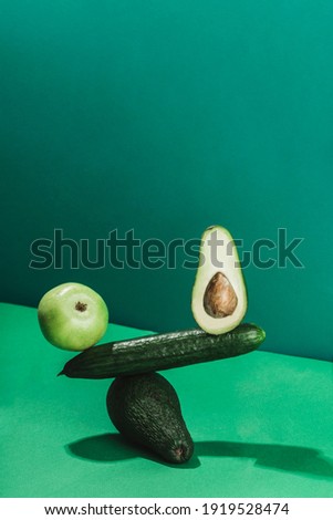the concept of a balance of fresh vegetables and fruits, cucumber, avocado and apple on a green background. vertical orientation with a copy space for the text.