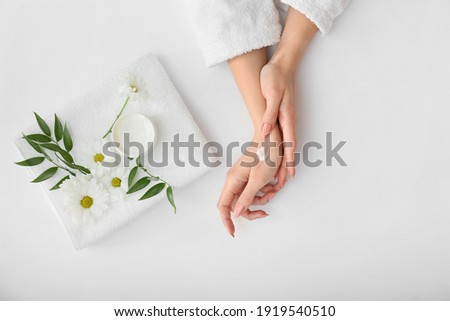 Female hands with cream, towel and beautiful flowers on light background Royalty-Free Stock Photo #1919540510