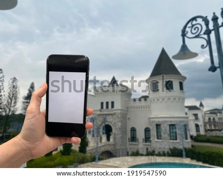 Human hand is holding phone for taking photo with blur castle background

