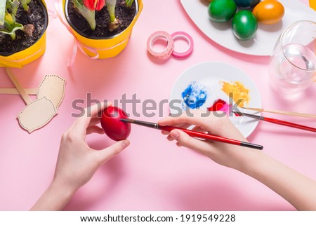 Woman hands painting Ester eggs on pink desk