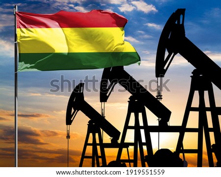 Oil rigs against the backdrop of the colorful sky and a flagpole with the flag of Bolivia. The concept of oil production, minerals, development of new deposits.