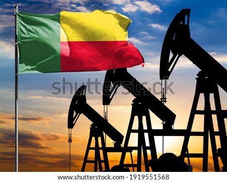 Oil rigs against the backdrop of the colorful sky and a flagpole with the flag of Benin. The concept of oil production, minerals, development of new deposits.