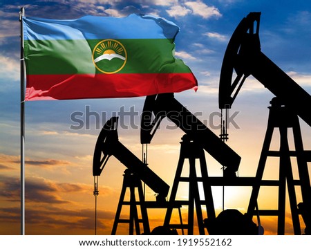 Oil rigs against the backdrop of the colorful sky and a flagpole with the flag of Karachay Cherkessia. The concept of oil production, minerals, development of new deposits.