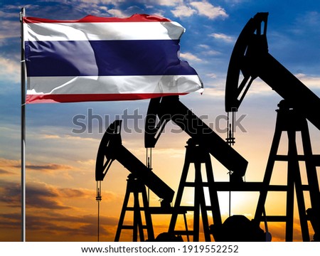 Oil rigs against the backdrop of the colorful sky and a flagpole with the flag of Thailand. The concept of oil production, minerals, development of new deposits.
