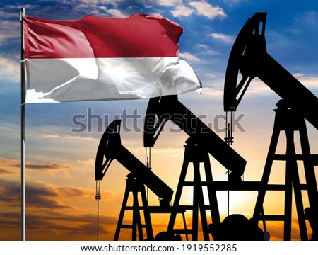Oil rigs against the backdrop of the colorful sky and a flagpole with the flag of Indonesia. The concept of oil production, minerals, development of new deposits.