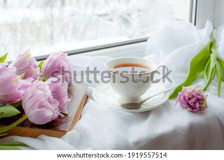 a mug of tea an old book a bouquet of tulips on the window