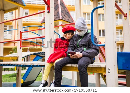 Schoolboy and preschool girl sitting on a playground and watching smartphone. Children watching cartoon instead of playing active outdoor games.