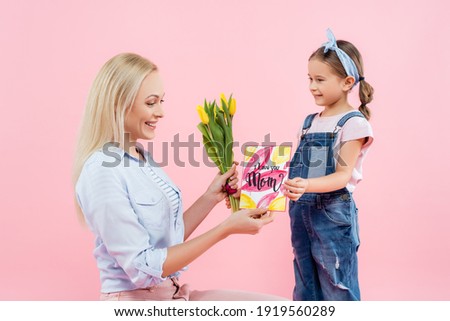 happy kid holding tulips and greeting card with i love you mom lettering near mother isolated on pink