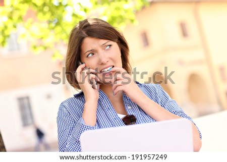 A picture of a worried woman with laptop talking on the phone in the park