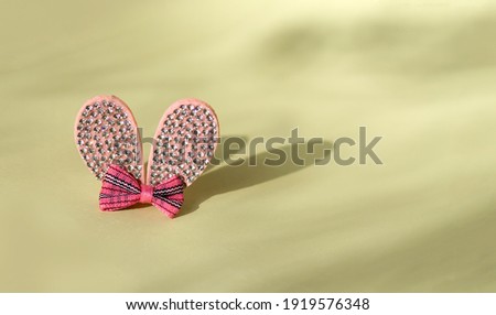 Rabbit ears with rhinestones and a bow on a pastel yellow background The ears cast a shadow, beautiful light and shadow pattern. Easter bunny ears
