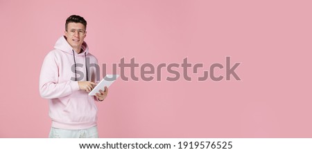 Pointing on tablet. Caucasian man's portrait isolated on pink background with copyspace. Handsome male model in street style. Concept of human emotions, facial expression, sales, ad, fashion. Flyer