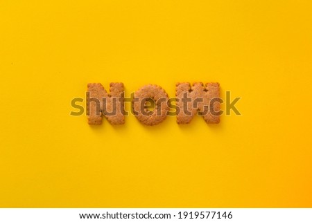 Word Now in the middle of the picture made of tasty crunchy cookies in the form of English alphabet letters, textured bright yellow background, health, dieting and medical concept. Copy space