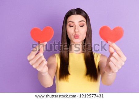 Portrait of attractive affectionate girl holding in hands two heart form sending air kiss isolated over violet purple pastel color background