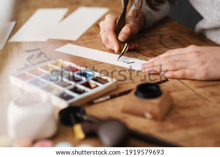 Calligrapher girl writing while working at table indoors Royalty-Free Stock Photo #1919579693