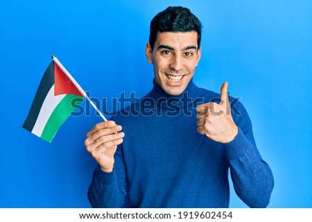 Handsome hispanic man holding jordania flag smiling happy and positive, thumb up doing excellent and approval sign 