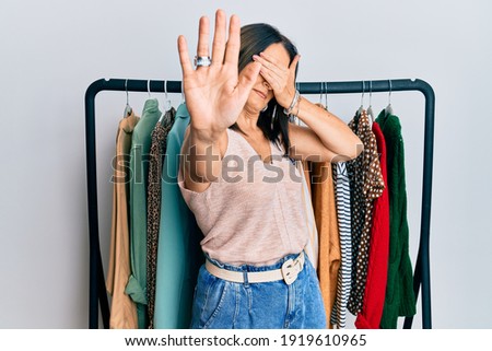 Middle age brunette woman working as professional personal shopper covering eyes with hands and doing stop gesture with sad and fear expression. embarrassed and negative concept. 