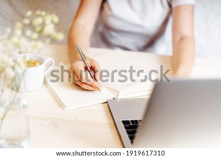 Distance learning online education and work. Business woman writes goals, plans, make to do and wish list in notebook on desk, working from home office. Using laptop. Royalty-Free Stock Photo #1919617310