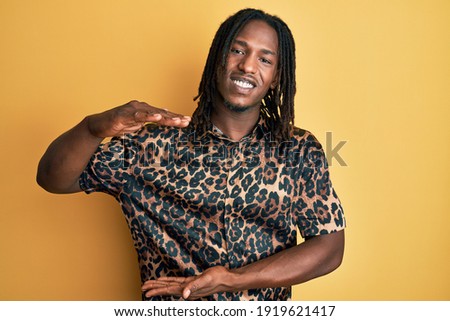 African american man with braids wearing leopard animal print shirt gesturing with hands showing big and large size sign, measure symbol. smiling looking at the camera. measuring concept. 