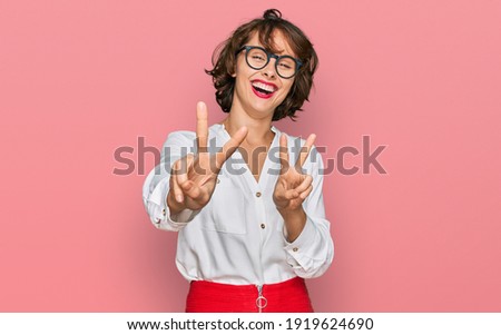 Young hispanic woman wearing business style and glasses smiling looking to the camera showing fingers doing victory sign. number two. 