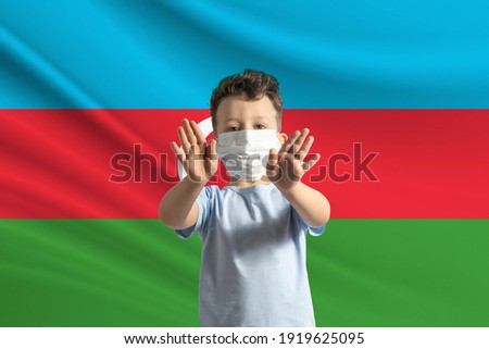 Little white boy in a protective mask on the background of the flag of Azerbaijan. Makes a stop sign with his hands, stay at home Azerbaijan.
