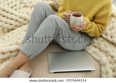 Woman with cup of tea and laptop sitting on sofa, closeup