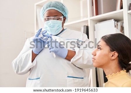 Have a look. Concentrated international nurse putting pipette and test tube at the protective place. Nurse hiding sample after testing. Coronavirus pandemic concept. Stock photo