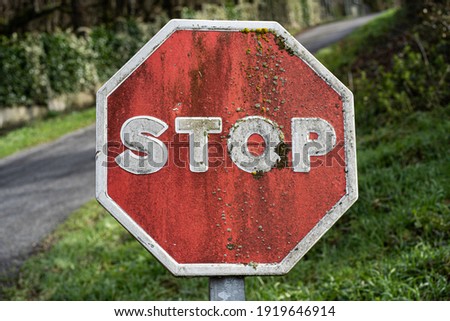 Stop sign deteriorated by humidity and moss, with a road in the background and green vegetation