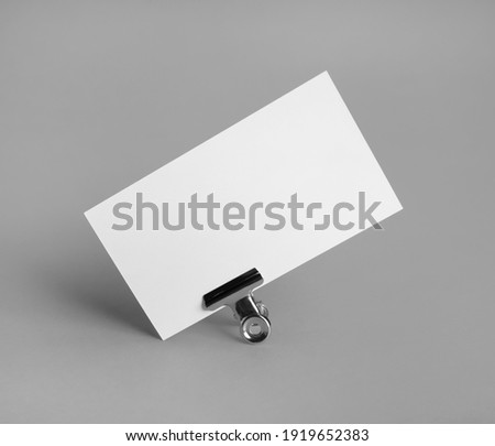 Photo of blank business card in metal binder clip on gray paper background.